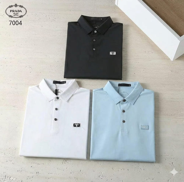 Three folded polo shirts in black, white, and light blue on a textured surface with Prada logo.
