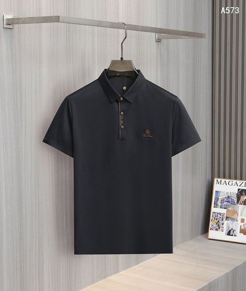 
men's polo shirt hanging on a wooden hanger against a gray textured wall. The shirt features a classic spread collar, a partial button placket with decorative striped trim, and a small embroidered logo on the left chest. A magazine display is visible in the lower right corner of the background.